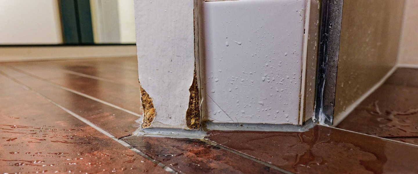 Water on a tile floor with a swollen door panel from moisture intrusion
